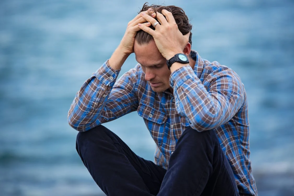 A man wearing a plaid shirt, holding his head