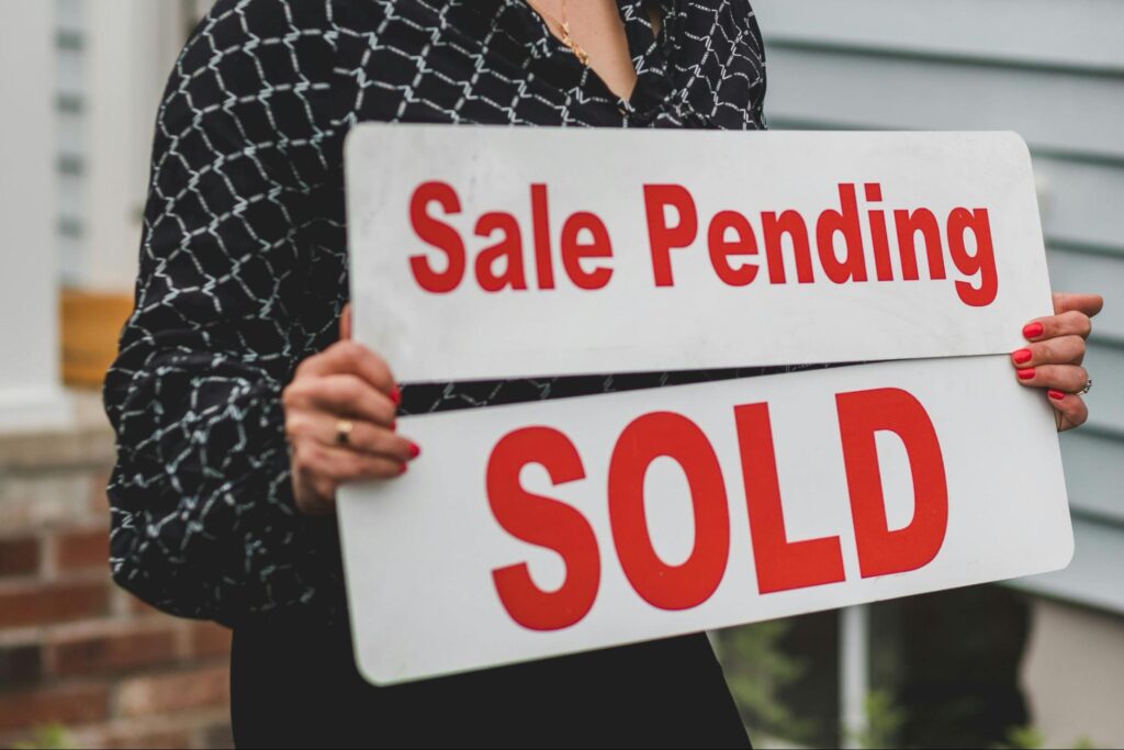 Woman holding signs saying “sale pending” and “sold”