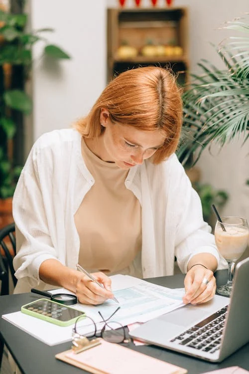 A woman making calculations with a laptop and smartphone