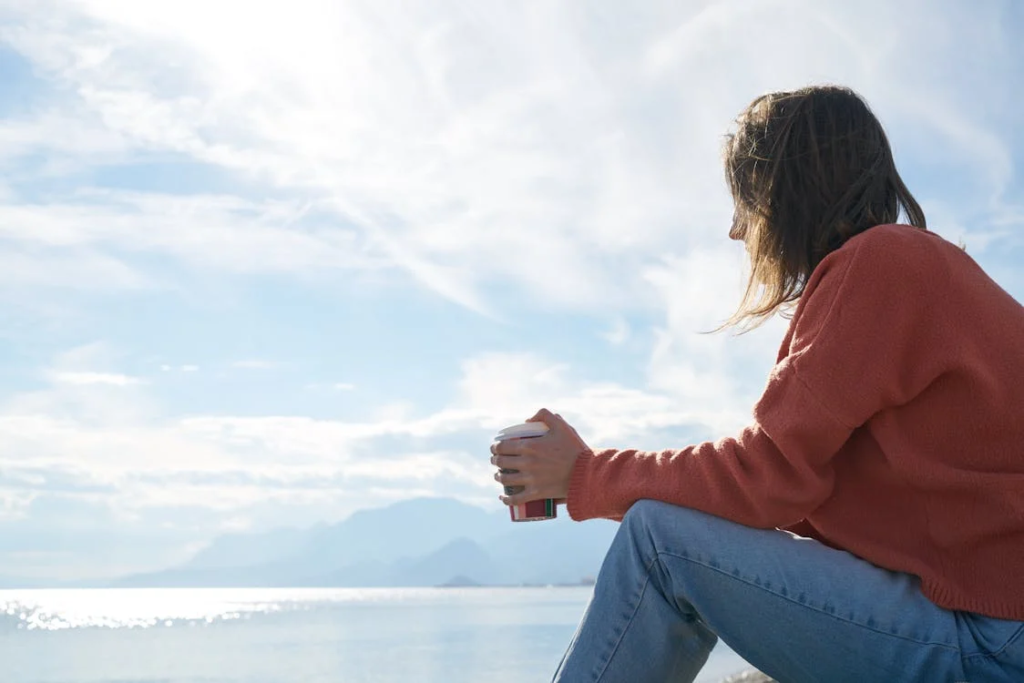 A woman holding a cup, sitting at a body of water