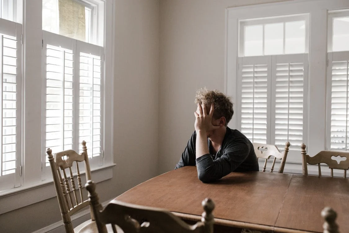 A man sitting at a wooden table, worried