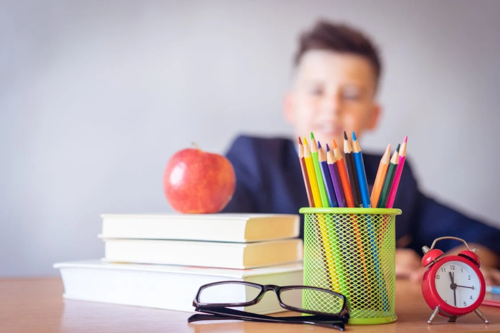 A boy sitting at a desk, with pencils, books, and an apple